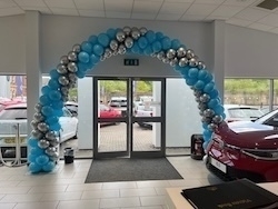 A festive balloon arch delivered ready made in blue and silver decorates the entrance of an indoor car showroom.