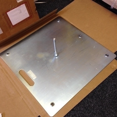 Auto-generated description: A metal plate with a bolt in the center rests in a cardboard box.