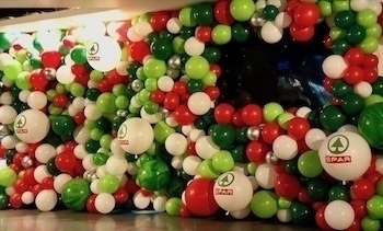 A festive wall display featuring an array of red, green, and white balloons, including several marked with the SPAR logo.