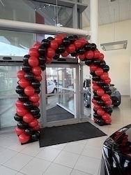 A red and black balloon arch delivered inflated in front of a glass doorway in a showroom.