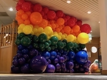 A vibrant balloon display forms a rainbow arch against a wall indoors.