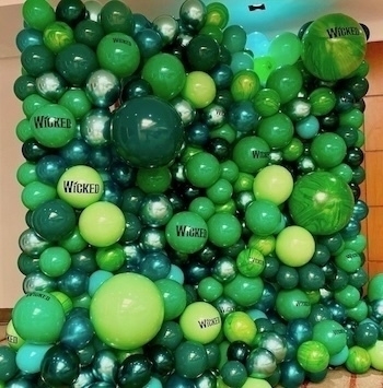 A wall filled with green and dark green balloons, some of which are labeled Wicked.